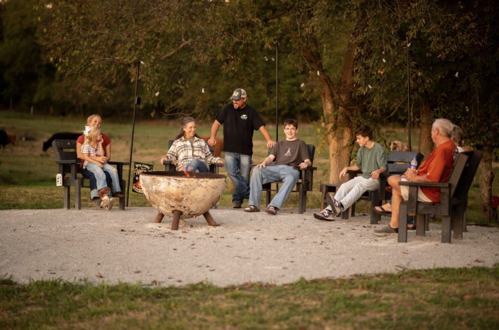 A group of visitors relaxing in chairs around an outdoor firepit.