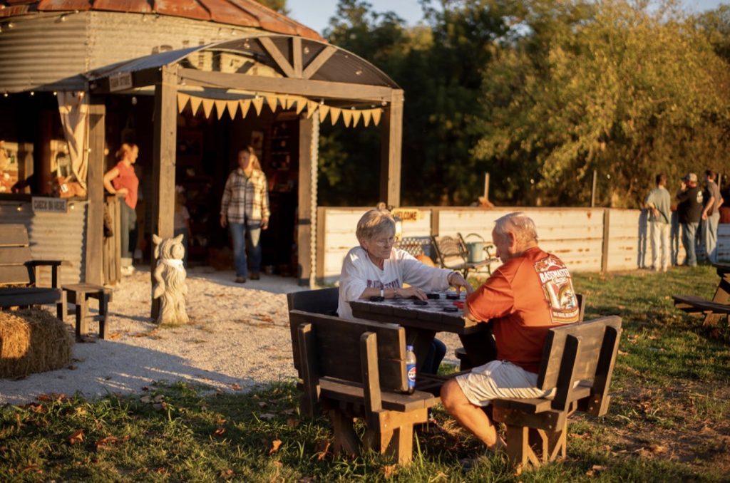 Visitors playing a tabletop game near the farm shop in golden evening light.