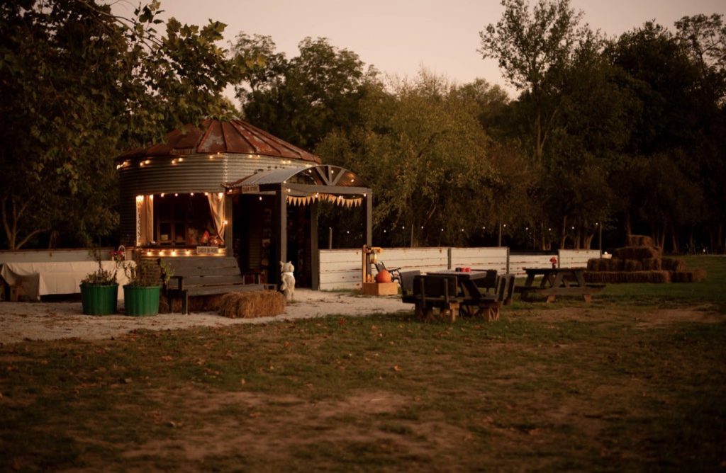 The round farm shop lit with string lights at dusk, with picnic tables outside.
