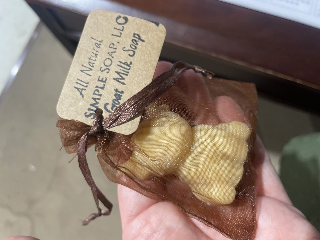 A hand holding goat milk soap in a brown organza bag with a paper label.