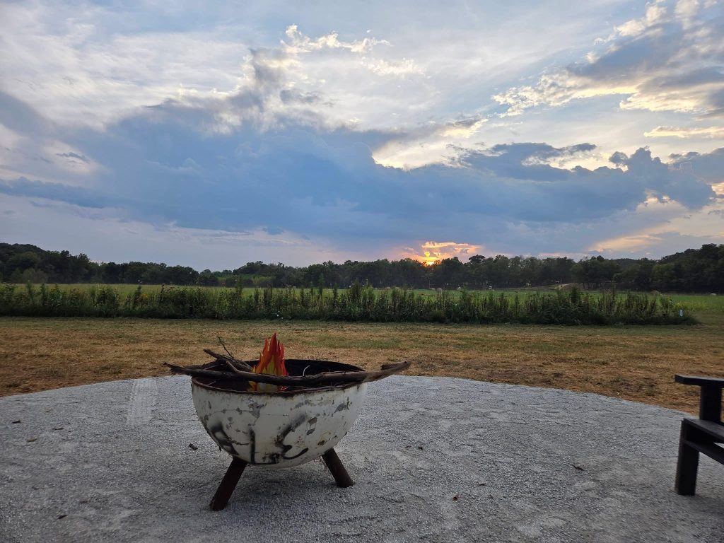 A metal fire bowl on a gravel patio with open pasture and an evening sky beyond.